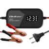 Na zdjęciu znajduje się inteligentna ładowarka z wyświetlaczem pokazującym "12.3" oraz tekstem "Qoltec SMART BATTERY CHARGER". Obok ładowarki widoczne są dwa zaciski w kolorze czerwonym i czarnym oraz wtyczka z dwoma bolcami.