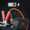 Na zdjęciu znajduje się inteligentna ładowarka z wyświetlaczem pokazującym "12.3 V A %", z logo "Qoltec" oraz napisem "SMART BATTERY CHARGER". Obok ładowarki widoczne są zaciski kabli podłączone do akumulatora, a nad nimi ikona baterii i błyskawicy.