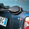 Na zdjęciu widać szczotkę rotacyjną czyszczącą przednią szybę samochodu, pokrytą pianą i wodą. Szczotka ma czarne włosie i jest przymocowana do czarnego uchwytu, a na szybie widoczne są ślady mycia.