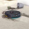 Na zdjęciu znajduje się granatowy robot sprzątający na jasnej podłodze, zbierający rozsypaną ziemię obok przewróconej doniczki i małego kaktusa. Na robocie widoczny jest napis "PHILIPS".