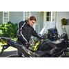 Na zdjęciu znajduje się motocykl, na którym umieszczone jest urządzenie rozruchowe w kolorze zielonym z widocznym logo "RYOBI". W tle widać fragment budynku z białymi drzwiami i oknami oraz roślinność.