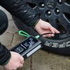 Osoba trzyma urządzenie rozruchowe GREEN CELL PowerBoost Air, które jest podłączone do opony samochodowej. Na wyświetlaczu urządzenia widoczne są cyfry oraz napis "ING GREEN CELL".