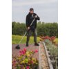 Mężczyzna trzymający metalową szczotkę na tarasie z kostki brukowej, otoczony kwitnącymi roślinami i zielonym krajobrazem w tle. Na zdjęciu widoczne są różowe kwiaty oraz krzewy, a w oddali znajduje się las.