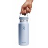 Niebieska butelka termiczna z logo Hydro Flask na przodzie, trzymana za uchwyt przez dłoń. Na butelce widoczny jest napis "Hydro Flask".