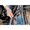 Na zdjęciu widoczna jest osoba zakładająca zapięcie rowerowe na przednie koło roweru. Na oponie znajduje się tekst: "47-622 28x1.75 28x1.50 700x45C".
