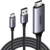 Na zdjęciu widoczne są trzy złącza kabla: HDMI, USB Typ-C i USB, każde z metaliczną obudową z napisem "UGREEN". Kabel ma plecioną osłonę, co sugeruje jego wytrzymałość.