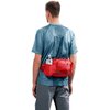 Mężczyzna ubrany w niebieską koszulkę i szare spodnie nosi czerwoną saszetkę z widoczną butelką, na której znajduje się logo "deuter". Saszetka ma kilka kieszeni i jest umieszczona na plecach.