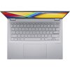 Srebrny laptop z widoczną klawiaturą QWERTY, dużym touchpadem i częściowo otwartym ekranem, na którym widać kolorowy pasek oraz napis "ASUS Vivobook". Na obudowie znajduje się subtelne logo "harman/kardon".