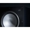 Zbliżenie na czarny subwoofer z widocznym głośnikiem i logo "polk" na obudowie. Obudowa ma matowe wykończenie z widocznymi śrubami mocującymi.