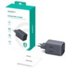 Szara ładowarka sieciowa z dwoma portami USB-C i napisem "100W" leży obok pudełka z napisem "AUKEY Comet Mix 3 100W PD Wall Charger with GaN Technology". Obok ładowarki znajduje się instrukcja obsługi z napisem "AUKEY USER MANUAL Comet Mix 3 100W".