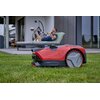 Czerwony robot koszący znajduje się na trawie przed nowoczesnym budynkiem z dużymi oknami. Na robocie widoczny jest napis: "PURE POWER FREELEXO CAM".