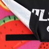 Fragment koca piknikowego z kolorowym wzorem przypominającym owoce, z widocznymi czerwonymi i zielonymi elementami. Na czarnym materiale znajduje się częściowo widoczny biały napis "NILS".