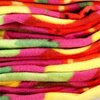 Stos materiału w intensywnych kolorach, takich jak różowy, czerwony, żółty i zielony, tworzy wzór przypominający owoce. Materiał jest miękki i puszysty, co sugeruje, że jest to koc piknikowy.