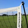 Na zdjęciu widoczny jest fragment bramki do piłki nożnej z białą taśmą, na której znajduje się napis "QUICKPLAY". W tle rozciąga się zielone boisko pod błękitnym niebem z kilkoma chmurami.