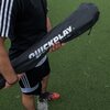 Osoba trzyma czarną torbę z białym napisem "QUICKPLAY" na tle zielonego boiska piłkarskiego. Na torbie widoczny jest również napis "SPOT 1 x 1.5M".