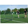Na zdjęciu znajduje się trenażer do piłki nożnej QUICKPLAY Pro Rebounder o wymiarach 150 x 150 cm, ustawiony na boisku piłkarskim. W tle widoczne są drzewa, ogrodzenie i fragmenty bramek piłkarskich.