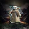 Trójwymiarowe puzzle przedstawiają postać z dużymi uszami i oczami, ubraną w szatę, stojącą na podstawce z napisem "Star Wars Grogu". W tle widoczne są rozmyte elementy krajobrazu.