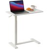 Na zdjęciu znajduje się biały stolik pod laptopa z regulowaną wysokością, na którym stoi otwarty laptop, filiżanka kawy oraz talerz z rogalikiem i owocami. Stolik ma prostą konstrukcję z płaską podstawą.
