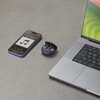 Na zdjęciu widoczny jest otwarty futerał z czarnymi słuchawkami dousznymi, obok leży smartfon z wyświetlaczem pokazującym ikonę nuty oraz godzinę 12:50, a także fragment laptopa z widoczną klawiaturą.