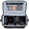 Torba fotograficzna w kolorze czarno-szarym z otwartą klapą, ukazująca wnętrze z trzema przegrodami, w których znajdują się aparat, obiektyw i dron. Na wewnętrznej stronie klapy widoczna jest siatkowa kieszeń z kablem, pomarańczowym narzędziem i dekielkie