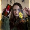 Osoba trzyma w jednej ręce telefon z wyświetlonym na ekranie tekstem: "3mk MOTOROLA MOTO G55", a w drugiej ręce przezroczystą płytkę z żółtym wzorem przypominającym rozlaną farbę. Tło jest rozmyte, a na nim widoczne są niewyraźne litery.