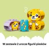 Na zdjęciu widoczne są kolorowe klocki LEGO DUPLO, przedstawiające elementy z motywem piesków oraz niebieski klocek z rysunkami kości. Na dole zdjęcia znajduje się tekst: "W zestawie 2 urocze figurki piesków".