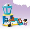 Na zdjęciu widoczne są klocki LEGO DUPLO, w tym żółty samolot, różnokolorowe klocki oraz figurki. Na niebieskim tle rozłożone są także akcesoria, takie jak walizki i książeczki z obrazkami.