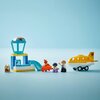 Zestaw LEGO DUPLO przedstawia scenę na lotnisku z żółtym samolotem, wieżą kontrolną i różnymi akcesoriami, takimi jak walizki i figurki. Na wieży kontrolnej widoczne jest logo z czerwonym samolotem na tle niebieskiego nieba.
