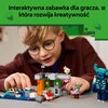 Na zdjęciu widoczny jest zestaw klocków LEGO przedstawiający scenę z gry Minecraft, zbudowany na szarej powierzchni. W górnej części zdjęcia znajduje się zielony pasek z tekstem: "Interaktywna zabawka dla gracza, która rozwija kreatywność".