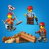 Na niebieskim tle znajdują się trzy figurki LEGO w czerwonych kaskach, ubrane w stroje robocze, trzymające narzędzia i znak drogowy. Przed nimi leży stos brązowych i beżowych klocków LEGO, przypominających cegły.