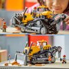 Na zdjęciu znajduje się żółty buldożer z klocków LEGO, z widocznymi gąsienicami i ruchomą łyżką, a obok niego stoją dwie figurki w kaskach. W tle widoczny jest znak ostrzegawczy z symbolem prac drogowych oraz kilka klocków imitujących cegły.