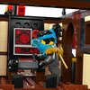 Na zdjęciu znajduje się wnętrze konstrukcji z klocków LEGO, przedstawiające panel sterowania z czerwonymi i niebieskimi elementami oraz ekranem z czerwonymi grafikami. Obok panelu stoi figurka LEGO w niebieskiej opasce, trzymająca złoty miecz na plecach.