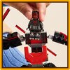 Na zdjęciu znajduje się zestaw klocków LEGO przedstawiający mecha z figurką w czarno-czerwonym stroju. W tle widoczna jest ręka trzymająca figurkę oraz fragment niebieskiego materiału.