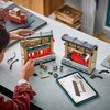 Na zdjęciu widać zestaw klocków LEGO przedstawiający scenę z pociągiem, złożony z dwóch segmentów, oraz rozłożone elementy i figurki na stole. Obok znajduje się tablet z instrukcją budowy, a na jednym z elementów widoczny jest napis "9 3/4".