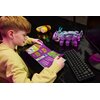 Na zdjęciu widać osobę siedzącą przy biurku, trzymającą telefon i patrzącą na instrukcję zestawu LEGO z napisem "LEGO Fortnite". Na biurku znajduje się złożony model LEGO, kilka rozrzuconych klocków oraz słuchawki.
