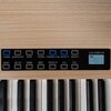 Na obrazie widoczny jest panel sterowania pianina cyfrowego z przyciskami oznaczonymi napisami: "POWER", "START/STOP", "SYNC", "CHORD", "TONE/RHYTHM", "SELECT+", "SELECT-", "RESET", "SET UP", "DEMO", "BEAT", "REC/PLAY", "VOL+", "VOL-". Obok przycisków zna