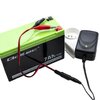Na zdjęciu znajduje się akumulator z widocznym logo "Qoltec" oraz oznaczeniem "7Ah/12V Rechargeable Lead Acid Battery (AGM)", do którego podłączone są przewody z klipsami. Obok akumulatora znajduje się ładowarka z zieloną diodą, podłączona do gniazdka ele