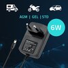 Na zdjęciu znajduje się inteligentna ładowarka z wtyczką do gniazdka, z widocznym napisem "QOLTEC CHARGER LEAD-ACID BATTERY" oraz oznaczeniami "AGM | GEL | STD" i "6W". W tle znajdują się ikony pojazdów oraz grafika z niebieskimi liniami i kropkami.