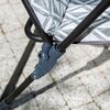 Zbliżenie na fragment fotela ogrodowego z metalową ramą i wzorzystym materiałem w odcieniach szarości. Widoczny jest mechanizm łączenia elementów ramy na tle brukowanej powierzchni.