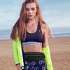 Osoba stoi na plaży, ubrana w sportowy strój, z czarną saszetką TECH-PROTECT M7 na biodrach. W tle widać piasek i morze pod jasnym niebem.