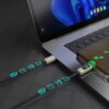 Na zdjęciu widać laptopa z podłączonym kablem USB-C - USB-C, który ma wyświetlacz LCD pokazujący "100". Kabel jest czarny, a na jego powierzchni widoczne są niebieskie ikony symbolizujące różne funkcje.