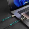 Na zdjęciu widać laptopa z podłączonym kablem USB-C - Lightning, który ma wyświetlacz LCD pokazujący "12". Kabel jest czarny, pleciony, a na jego powierzchni widoczne są niebieskie ikony symbolizujące różne funkcje.