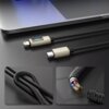 Na zdjęciu znajduje się czarny kabel USB-C - Lightning z wyświetlaczem LCD, podłączony do laptopa, z widocznymi szczegółami konstrukcji kabla, takimi jak pleciona osłona i odsłonięte przewody. Wyświetlacz na kablu pokazuje wartość "20W".