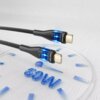 Na zdjęciu widoczny jest czarny kabel USB-C - USB-C z podświetleniem LED, oznaczony napisem "VEN-DENS". W tle znajduje się przezroczysta tarcza z niebieskimi oznaczeniami i napisem "60W".