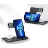 Na zdjęciu widoczna jest czarna ładowarka indukcyjna 3w1, na której umieszczone są smartfon, zegarek i etui na słuchawki, wszystkie z ikoną ładowania. Urządzenia są ustawione na podstawce z niebieskimi akcentami świetlnymi.