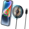 Na zdjęciu znajduje się czarna ładowarka indukcyjna z okrągłą powierzchnią, na której widoczny jest symbol błyskawicy, oraz smartfon z kolorowym ekranem i zieloną ikoną ładowania. Ładowarka jest podłączona do kabla z wtyczką USB-C.