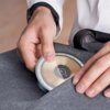 Na zdjęciu widać osobę wkładającą czarną ładowarkę indukcyjną z widoczną spiralą miedzianą do szarej torby. Na środku ładowarki znajduje się symbol błyskawicy.