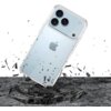 Przezroczyste etui na telefon z trzema dużymi obiektywami aparatu jest przedstawione w dynamicznej scenie, gdzie unosi się nad powierzchnią, z której unoszą się fragmenty materiału, sugerując uderzenie. Na etui widoczne jest logo w kształcie nadgryzionego