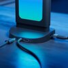Na zdjęciu znajduje się stacja dokująca z kilkoma podłączonymi kablami USB, umieszczona na powierzchni stołu. Urządzenie emituje niebieskie światło, a na jego podstawie widoczne są porty USB i USB-C.