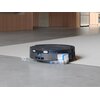 Czarny robot sprzątający ECOVACS Deebot T80 Omini znajduje się na granicy podłogi i dywanu, z widocznym oznaczeniem "10 mm" oraz strzałkami wskazującymi na jego zdolność pokonywania różnic wysokości. W tle widać kuchnię z drewnianymi szafkami i metalową l
